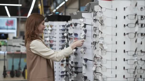 Negozi al dettaglio, bella ragazza acquirente sceglie occhiali da sole in un centro commerciale durante una vendita stagionale, donna felice in occhiali da sole gialli guardando in macchina fotografica, stile di vita — Video Stock