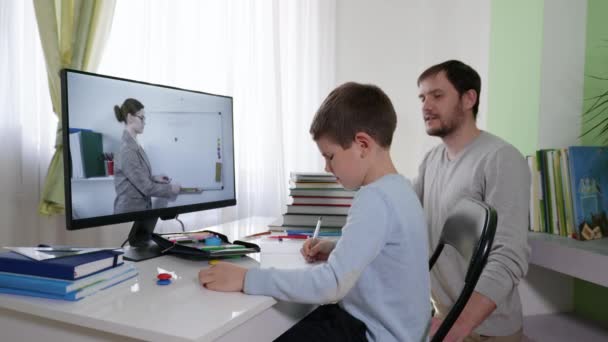 Loving father helps a male child learn online lessons during distance learning while sitting at home at a computer — Stock Video