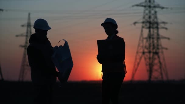 Silhouette, engineers at high-voltage power plant with laptop and drawings shake hands with each other and discusses plan for supply of electricity to city at sunset — Stock Video