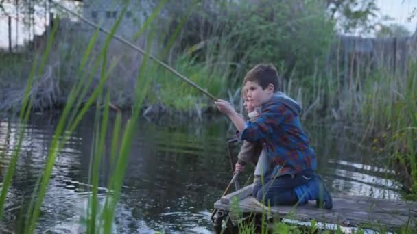 Αστείες διακοπές, αρσενικά παιδιά μικροί ψαράδες πιάνουν ψάρια με καλάμι ψαρέματος σε μια προβλήτα κοντά στο ποτάμι — Αρχείο Βίντεο