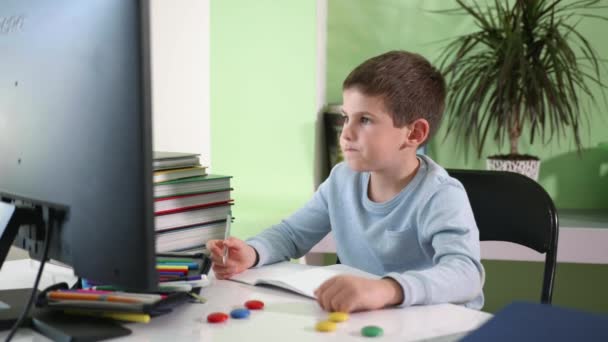 Aprendizaje a distancia, el niño se sienta en la pantalla del monitor y ve la lección de vídeo en línea — Vídeo de stock