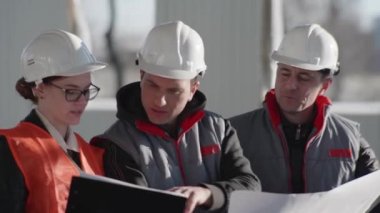 Elinde çizimler olan güvenlik kaskları uzmanlarından oluşan bir ekip, yeni bir iç hangarı tartışıyor.