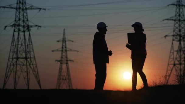Team of engineers in protective helmets with laptop in hands discuss energy efficiency and construction of high-voltage pylons and transmission towers — Stock Video