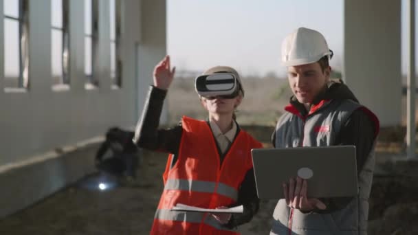 Modern inşaat, kadın ve erkek inşaat uzmanları VR gözlüklerinde gelişmiş teknoloji kullanırken, koruyucu miğferler yeni inşaat projesini ele alıyorlar — Stok video