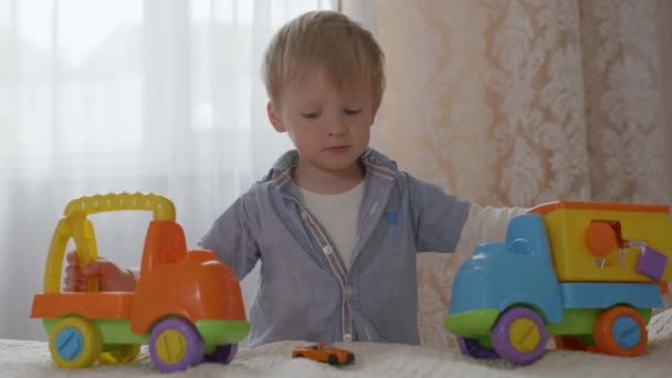 Χαριτωμένο ευτυχισμένο χαρούμενο αρσενικό παιδί με καλό νευρικό σύστημα και καλή υγεία διασκεδάστε παίζοντας με πλαστικά χρωματιστά παιχνίδια — Αρχείο Βίντεο