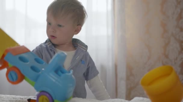 Zorgeloze kindertijd, aantrekkelijke vrolijke mannelijke kind spelen met plastic gekleurd speelgoed — Stockvideo