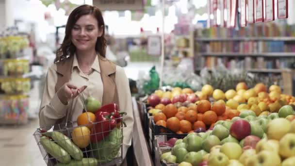 Ladenöffnung, Porträt einer schönen lächelnden Frau mit einem Einkaufskorb in der Hand kauft ökologisches Gemüse und Obst im Supermarkt — Stockvideo