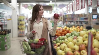 Düzgün beslenme, taze sebze ve meyvelerle dolu sepeti olan sağlıklı genç bir kız süpermarketten elma seçiyor.