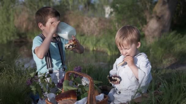 Przekąski, głodne dzieci dobrze się bawią jedząc pieczenie i pijąc mleko ze szklanego słoika — Wideo stockowe