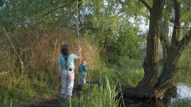 Весело времяпрепровождение, милые малыши унесли играть длинные палочки в зеленых деревьях на реке — стоковое видео