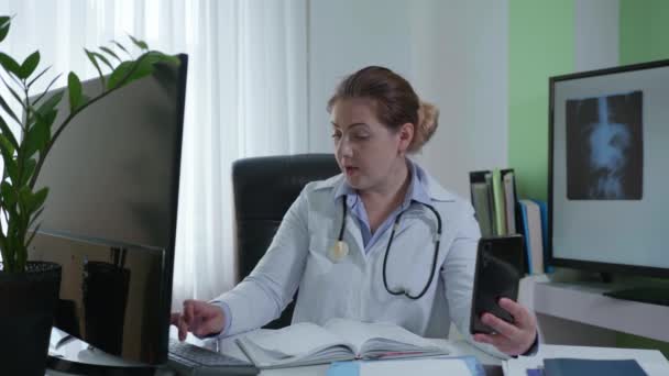 Médecine moderne, femme médecin communique avec le patient à l'aide d'un téléphone mobile, regarde les résultats des tests sur écran moniteurs et conseille une personne en ligne sur le traitement ultérieur — Video
