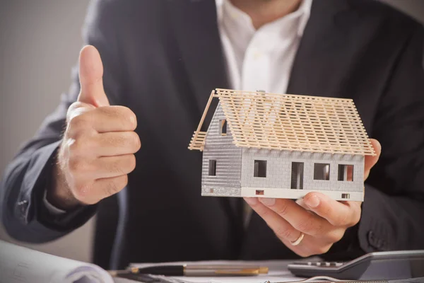 Businessman Holding Model House In Palm Of Hand