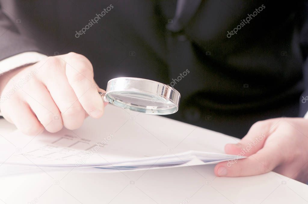 Close-up Of Young Businessman Hand Examining Invoice With Magnif