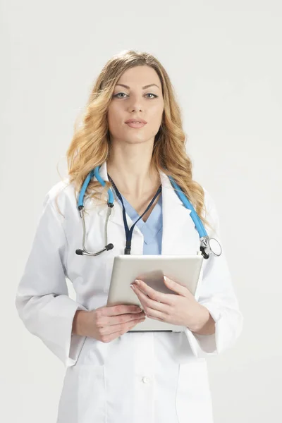 Femme médecin en manteau chirurgical blanc avec stéthoscope et comprimé dans les mains debout isolé sur fond blanc — Photo