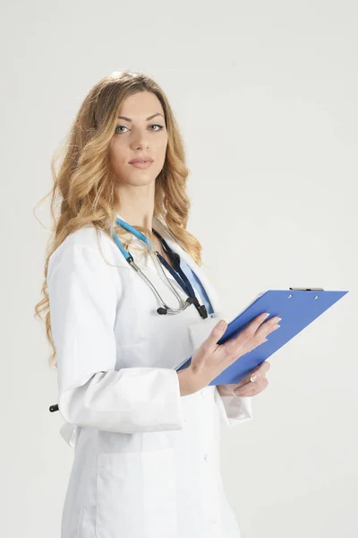 Γυναίκα γιατρός σε λευκό παλτό χειρουργική με στηθοσκόπιο και μπλε χαρτί holder σε χέρια στέκεται απομονωθεί σε λευκό φόντο — Φωτογραφία Αρχείου