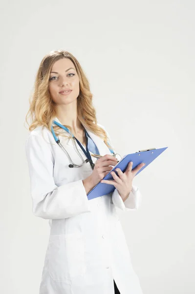 Médecin femme en manteau chirurgical blanc avec stéthoscope et porte-papier bleu dans les mains debout isolé sur fond blanc — Photo