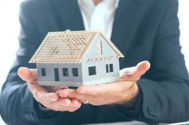 bir ev modeli ellerini avucunda tutan iş adamı