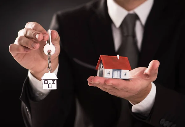 Агент по недвижимости держит ключ от дома, модель дома — стоковое фото