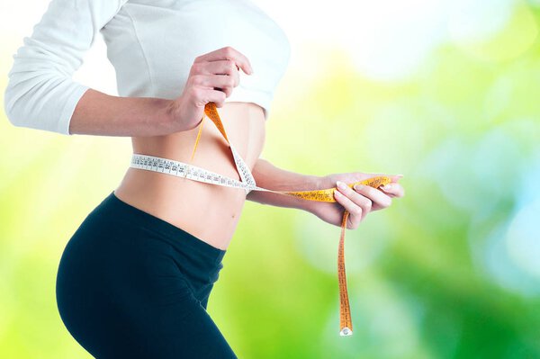 Slim young woman measuring her thin waist with a tape measure