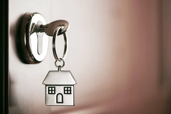 Chave da casa em uma casa em forma de chaveiro de prata na fechadura de um entr — Fotografia de Stock