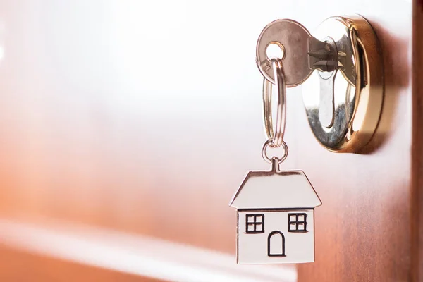 House key on a house shaped silver keyring in the lock of a entr — Stock Photo, Image