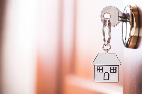 House key on a house shaped silver keyring in the lock of a entr — Stock Photo, Image