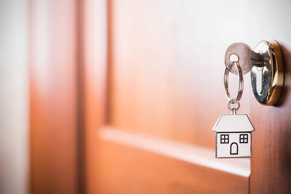 House key on a house shaped silver keyring in the lock of a entr — Stock Photo, Image