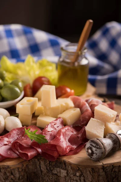 Assorted deli meats and a plate of cheese, on a wooden cutting b — Stock Photo, Image