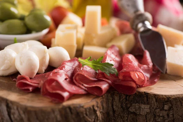 Assorted deli meats and a plate of cheese, on a wooden cutting b — Stock Photo, Image
