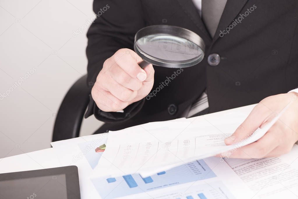 Businessman checking a tablet with magnifying glass 
