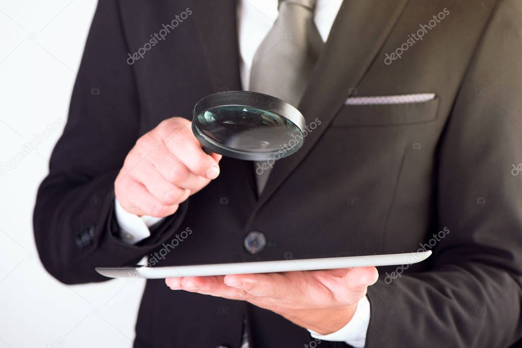 Businessman checking a tablet with magnifying glass 