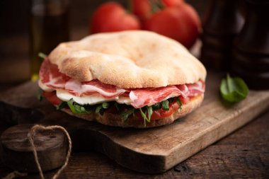 Arap ekmeğinden sandviç, marullu roka, taze domates dilimleri, peynir ve jambon. Kapat.