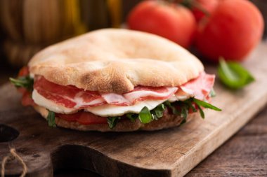 Arap ekmeğinden sandviç, marullu roka, taze domates dilimleri, peynir ve jambon. Kapat.