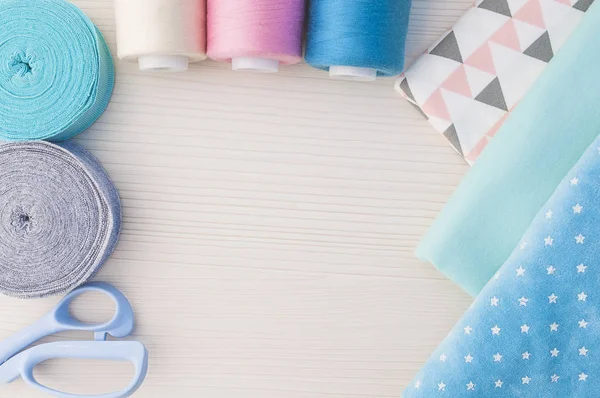 Швейный набор. Thread blue, pink, beige, cloth fabric, scissors, rolls ribana grey and menthol — стоковое фото
