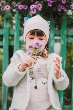 Küçük (genç) kız bir çiçek kokluyor. Yeşil fe bir arka plan üzerinde