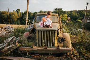 küçük kız bir bebek ile eski bir araba oturur