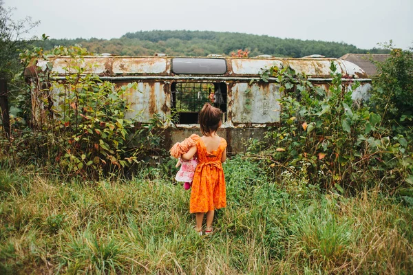Chica con una muñeca de pie cerca del viejo remolque — Foto de Stock