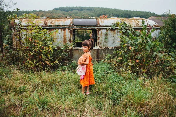 Chica con una muñeca de pie cerca del viejo remolque — Foto de Stock