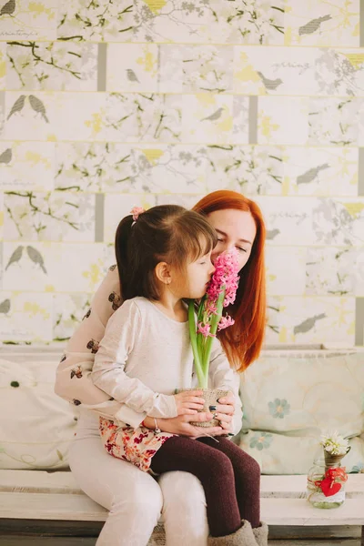 Annemin dizlerinin üzerinde oturan kız. çiçek koklama