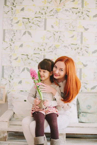 Annemin dizlerinin üzerinde oturan kız. çiçek koklama