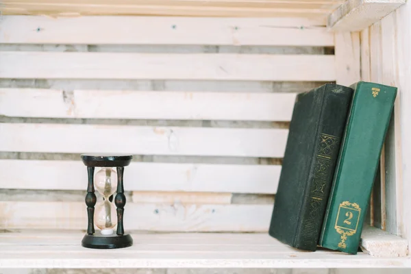 Old books and sand clock lie on a white shelf. — Stock Photo, Image