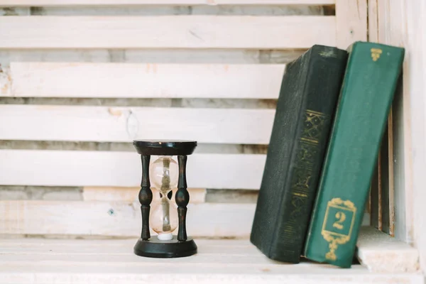 eski kitaplar ve kum saati beyaz bir rafa yalan