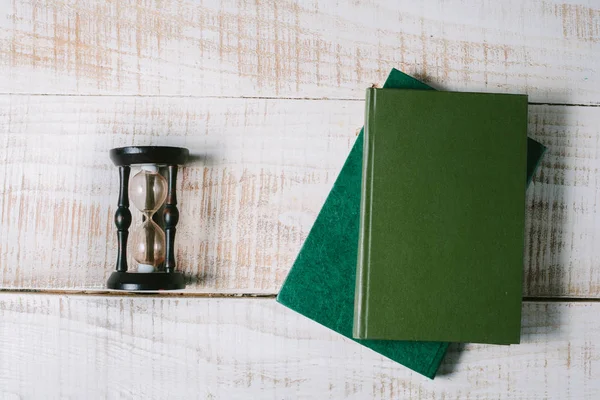 Green books and hourglasses lie on a wooden table. top view — Stock Photo, Image