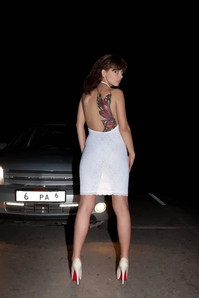 Fille en robe blanche dans les phares sur la route de nuit — Photo