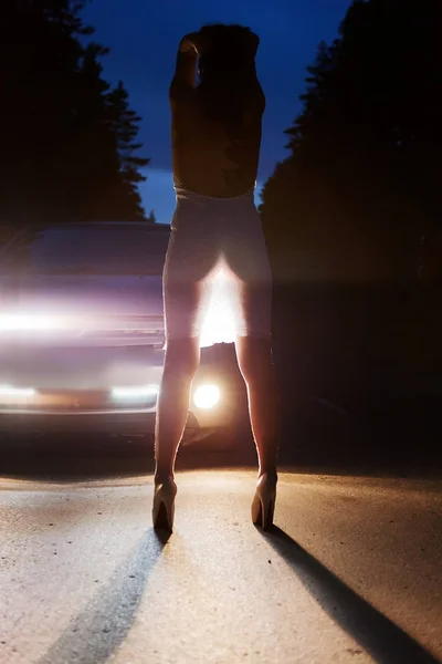Mädchen in weißem Kleid im Scheinwerferlicht auf der nächtlichen Straße — Stockfoto