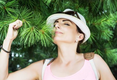 Young caucasian woman sniffs green needles of conifer tree clipart