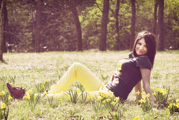Krásná mladá žena pózuje s žluté narcisy na louce — Stock fotografie