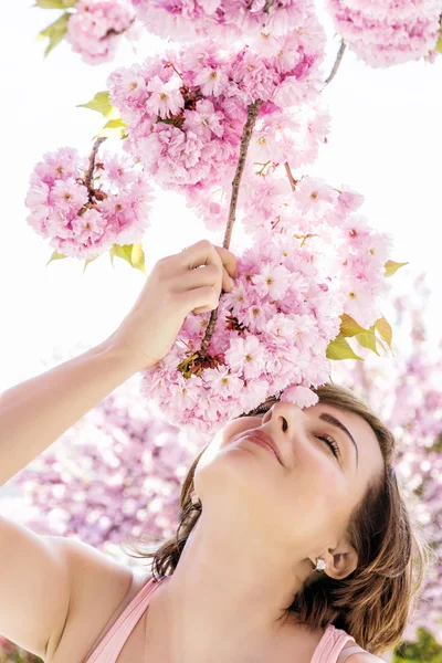 Žena sniffs větev sakura — Stock fotografie