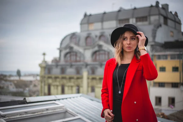 Дівчина в червоному і з чорним капелюхом позує на даху старого міста — стокове фото