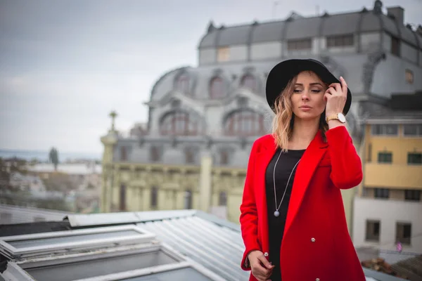 Дівчина в червоному і з чорним капелюхом позує на даху старого міста — стокове фото